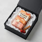 Angle : Vue de trois-quarts haut ($30^\circ$).Scène : Le carton de l'image image_8abcc7.jpg est délicatement couché à l'intérieur d'un coffret de présentation e-commerce premium ouvert. Il est niché au milieu de papier de soie froissé d'un blanc éclatant. Deux petites fraises des bois entières et un bâton de cannelle sont posés de manière artistique dans un coin pour compléter la composition de studio.Fond : Une surface de studio gris béton très clair et minimaliste. (gemini-3.1-flash-image-preview)