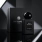 Angle : Prise de vue frontale, mettant en avant le design et le graphisme de la marque.  Fond : Un arrière-plan minimaliste et abstrait aux nuances de gris anthracite et noir mat.  Mise en scène : Une luxueuse boîte ou un coffret noir fermé "Gris Montaigne Paris" avec son logo floral argenté est placé à l'arrière. Juste devant, légèrement excentré, le flacon de parfum "Bois Montaigne" est posé, créant un reflet subtil sur un sol miroir noir brillant.  Lumière : Éclairage publicitaire de studio, faisceaux lu