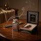 Un plan large à 45 degrés du coffret ouvert de image_1fe27b.jpg avec son flacon disposé juste à côté sur une table de présentation en bois précieux foncé. Une fine et gracieuse volute de fumée d'encens oriental ou de bakhoor traverse la composition de manière réaliste. L'éclairage est chaleureux et tamisé, créant une atmosphère de rituel de parfumage sacré. Style : Campagne éditoriale luxueuse. (gemini-3.1-flash-image-preview)