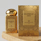 Un plan moyen net et rigoureusement frontal du coffret d'or mat image_2046de.jpg posé à la verticale sur une dalle de grès poli texturé de couleur ocre. La lumière de studio est directionnelle et chaude, venant de biais pour faire briller subtilement le motif mandala et l'inscription 'MAJORELLE GOLD' de image_2046de.jpg. L'arrière-plan est minimaliste et épuré pour concentrer toute l'attention sur la trame luxueuse du packaging. Style : Photographie publicitaire de haute joaillerie. (gemini-3.1-flash-image-