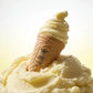 Un visuel haut de gamme au format carré de 1200x1200px. Le flacon de parfum de image_93d566.jpg émerge artistiquement à mi-hauteur d'une surface onctueuse et texturée de sorbet au citron jaune pâle parsemé de cristaux de glace givrés. L'arrière-plan est un dégradé de blanc pur à jaune citron très doux. Une lumière rasante de studio met en valeur les courbes de la volute supérieure et rend le texte de l'étiquette ultra-net. (gemini-3-pro-image-preview)