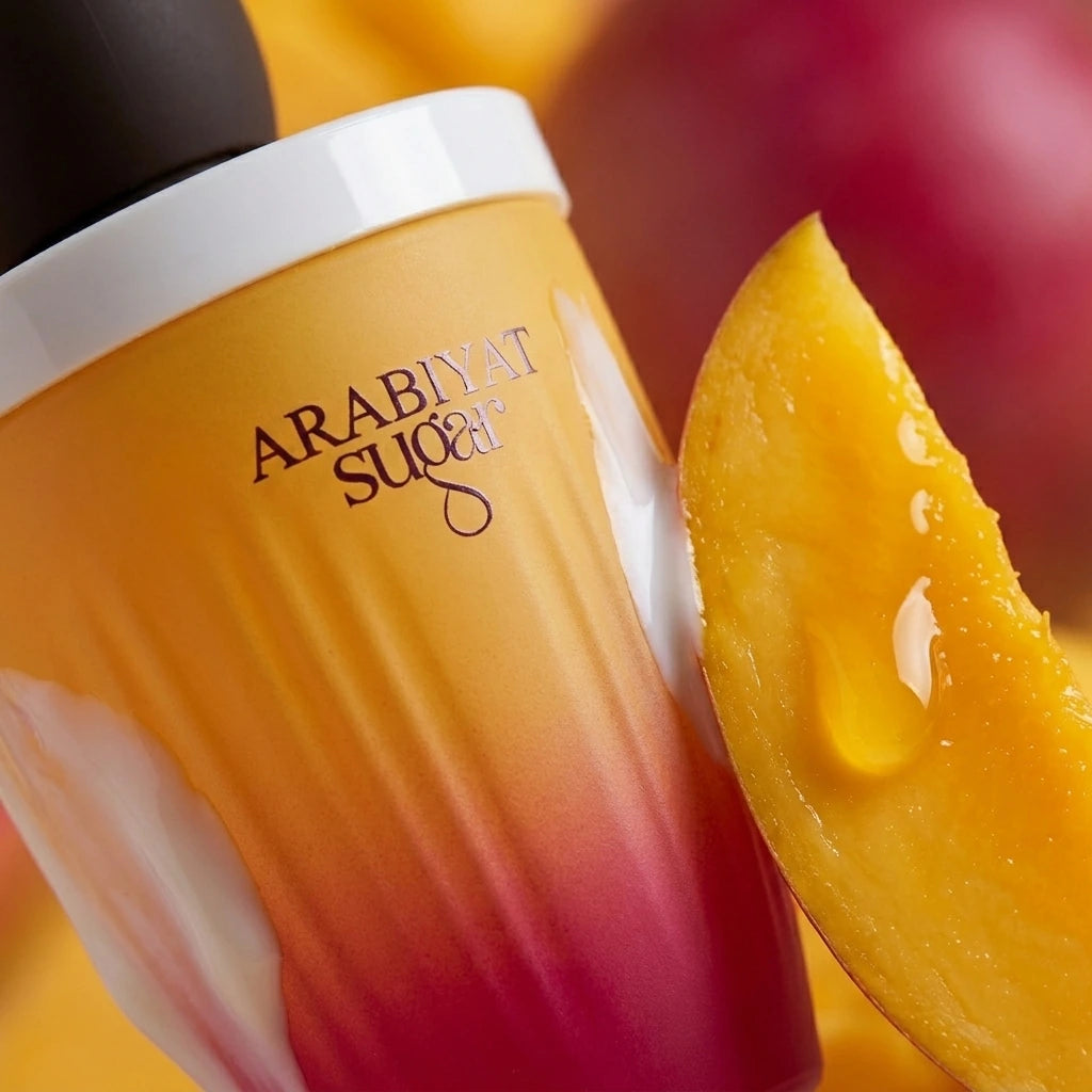Angle : Gros plan macro serré, angle à $45^\circ$ orienté vers la transition jaune-orange et fuchsia du flacon.Scène : Focus absolu sur le verre givré du flacon de "Mango Affogato" de l'image image_880a4d.jpg. Juste à côté, une tranche de mangue mûre et juteuse laisse perler une goutte de jus dorée translucide qui capte la lumière. Une fine volute de crème laiteuse frôle le flacon. L'éclairage de studio crée un reflet vertical parfait (softbox) sur la bague blanche et l'inscription "ARABIYAT SUGAR".Fond : A