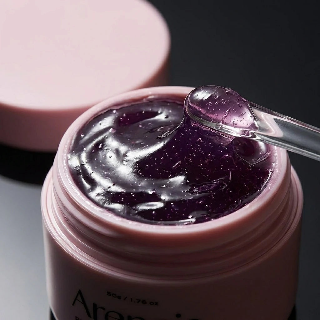 Angle : Gros plan macro très serré, focus sur la surface du gel ondulé.  Scène : Le pot d'Arencia de l'image image_cd743d.jpg est ouvert, révélant la texture gélifiée, pourpre et intensément brillante du sérum. Le couvercle mat rose est posé en arrière-plan, légèrement flouté. Une fine spatule en verre transparent est posée sur le rebord du pot, une pointe de gel brillant s'étirant depuis son extrémité.  Fond & Lumière : Arrière-plan minimaliste sombre. Un éclairage rasant de studio fait miroiter les ondula