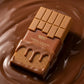 Angle : Macro à 45°  Gros plan du parfum Arabiyat Prestige Toffee Ganache posé dans une rivière de chocolat fondu brillant. Le chocolat épouse délicatement la base du flacon. Détails très nets, rendu ultra réaliste, photographie publicitaire premium. (gemini-3-pro-image-preview)