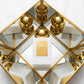 Un plan moyen en plongée à 60 degrés du flacon de image_7.png placé au centre d'une structure géométrique de miroirs dorés inclinés. Les miroirs reflètent à l'infini le capuchon doré et sphérique du flacon, créant un effet de couronne lumineuse. Le fond est une texture de lin blanc immaculé. Style : Composition artistique moderniste de studio. (gemini-3-pro-image-preview)