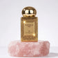 Un plan moyen net et frontal du flacon rectangulaire de image_2046de.jpg isolé de sa boîte, posé sur un bloc de quartz rose brut. La lumière de studio frappe le flacon de face pour faire scintiller chaque détail du motif mandala doré gravé sur la bouteille de image_2046de.jpg. Le bouchon sphérique en or poli capte un reflet miroir linéaire parfait de l'environnement de studio. Style : Photographie cosmétique de haute précision. (gemini-3-pro-image-preview)