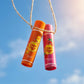High-end commercial product photography, dramatic low angle view looking up at a Chupa Chups "Orange Pop & Strawberry Swirl" lip balm suspended in mid-air by a thin, rustic twine string. Background is a clear, bright summer sky with a subtle sun flare. Sharp focus on the product branding, photorealistic, crisp details, no CGI --ar 1:1 (gemini-3-pro-image-preview)