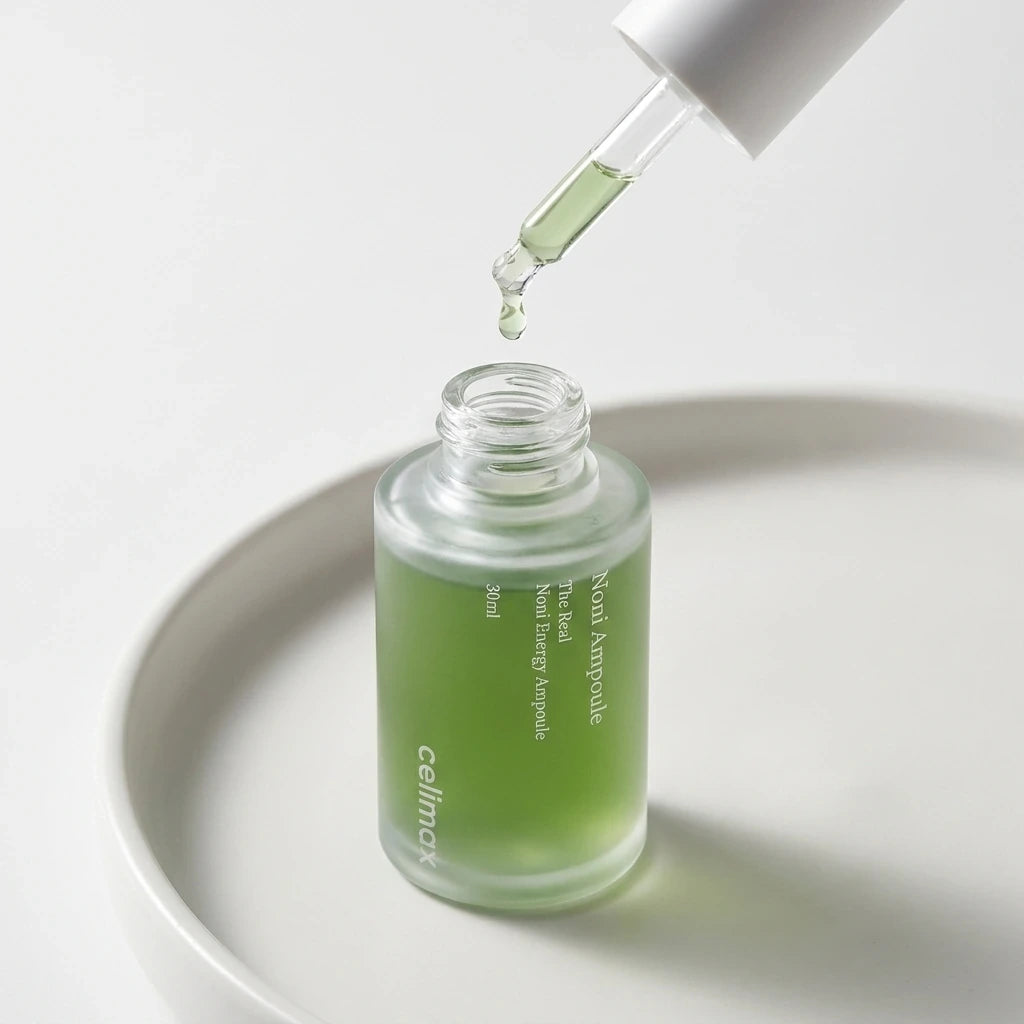 High-end commercial cosmetic photography of the Celimax Noni Energy Ampoule. The bottle is placed on a smooth, matte white ceramic surface. The dropper is extracted and held just above the bottle opening, with one single, clear, slightly viscous drop of the liquid serum about to fall. Soft, diffused studio lighting creating gentle shadows. Minimalist aesthetic. Shot on 70mm lens, F7 aperture, ISO 250. Photorealistic, macro details, ultra-sharp focus on the drop. --ar 1:1 (gemini-3-pro-image-preview)