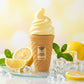 Creative e-commerce shot of the Arabiyat Sugar Lemon Sorbet perfume bottle inspired by image_520fa2.jpg. The bottle stands elegantly on a frosted glass surface, surrounded by fresh juicy lemon slices, mint leaves, and crystal-clear crushed ice cubes scattering subtle reflections. The background is a soft, sun-drenched pastel yellow and white blurred bokeh gradient. Vibrant, zesty, and sweet fragrance concept. Aspect ratio 1:1, size 1200x1200px. (gemini-3-pro-image-preview)