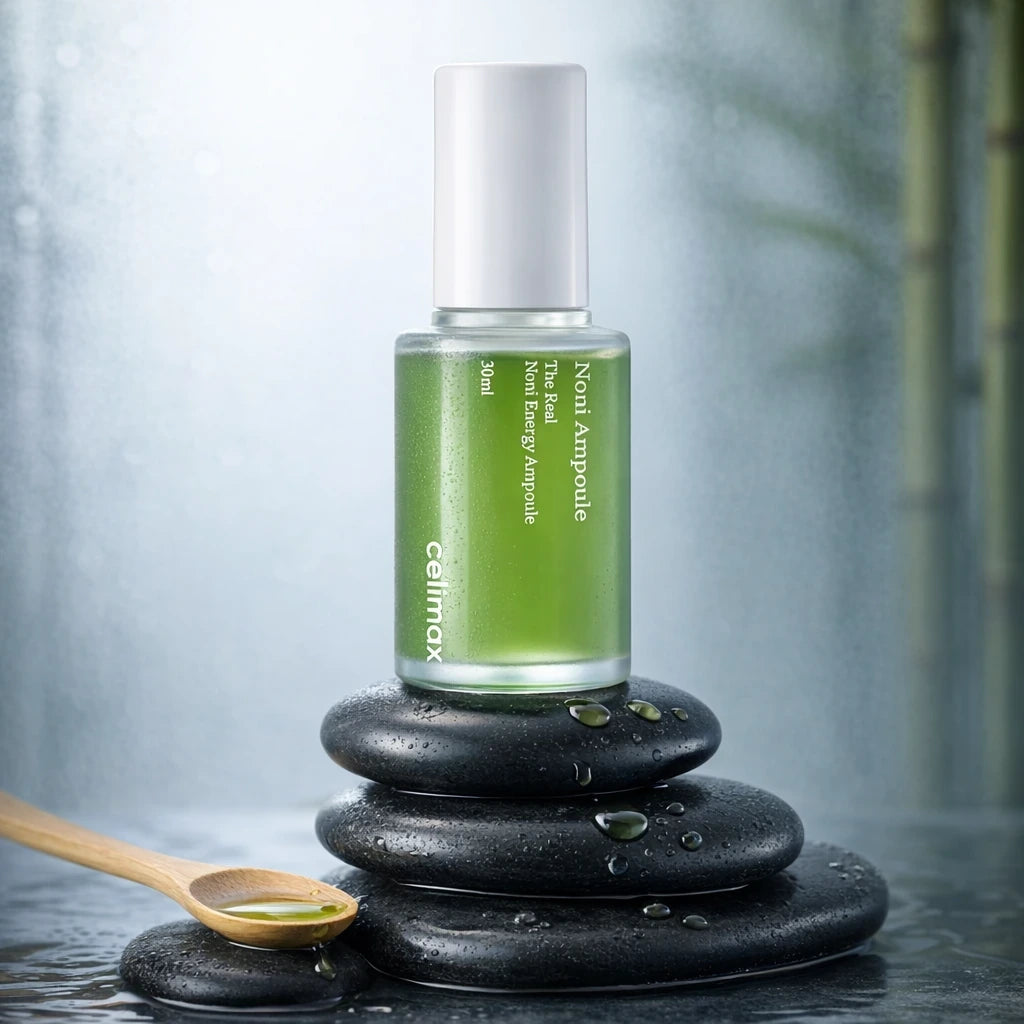 Still life commercial photography, spa aesthetic. The Celimax Noni Energy Ampoule is balanced on a stack of smooth, dark, wet zen river stones. Beside them is a small bamboo spoon holding a small amount of the liquid ampoule, and a few drops are spilled artfully on the stones. Background is softly blurred steamed glass and bamboo. Cool, calming lighting. High realism, tactile textures. Shot on 70mm lens, F7 aperture, ISO 250. --ar 1:1 (gpt-image-1.5)